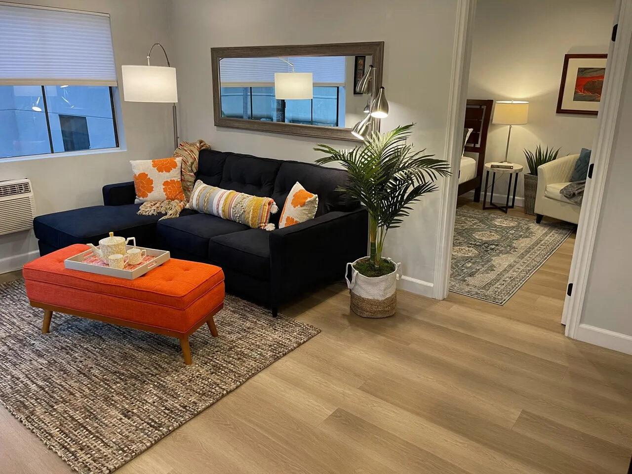 Living room with navy sofa, orange accents, and open bedroom view in the Hillcrest apartment
